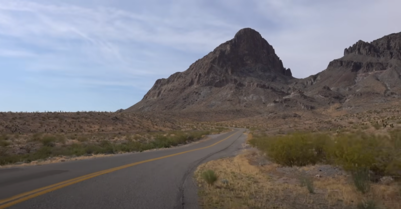 A Scenic View of Route 66 Winding Through a Desert Landscape with Towering Rocky Mountains and Sparse Vegetation Under a Clear Sky